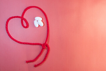 Horizontal top view of red string in the shape of a heart with white tablets