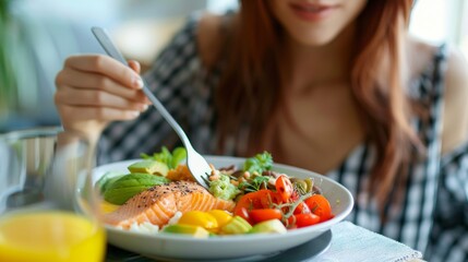 Naklejka premium A woman sits at a table and enjoys a meal of fresh salmon, avocado, tomatoes, and salad