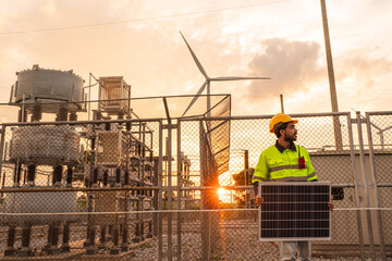 Engineer wearing uniform holding solar panels and inspection work in wind turbine farms at sunset rotation to generate electricity energy. Alternative energy concept.