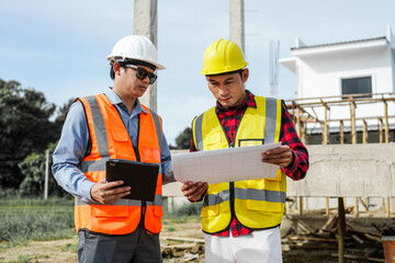 Two male construction workers, including an Asian engineer, meticulously review structural plans and design concrete columns and beams for a new residential build.