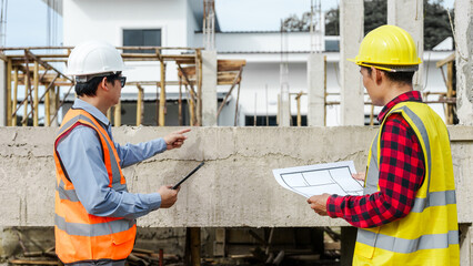 Two male construction workers, including an Asian engineer, meticulously review structural plans...