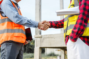 Two male construction workers, including an Asian engineer, meticulously review structural plans...