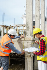 Two male construction workers, including an Asian engineer, meticulously review structural plans...