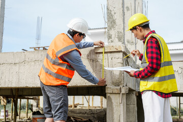Two male construction workers, including an Asian engineer, meticulously review structural plans and design concrete columns and beams for a new residential build.