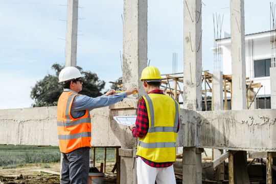 Two male construction workers, including an Asian engineer, meticulously review structural plans and design concrete columns and beams for a new residential build.