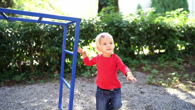 Little girl trying to climb the monkey bars on the playground. High quality 4k footage