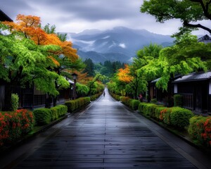 Obraz premium A serene, wet pathway lined with vibrant trees and traditional houses, leading towards misty mountains in the background.