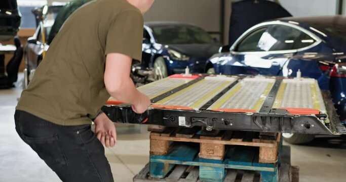 Technician repairing an electric car battery module in a modern workshop. High voltage lithium-ion battery pack on production line. Electric car. Pack of battery cells module. EV car