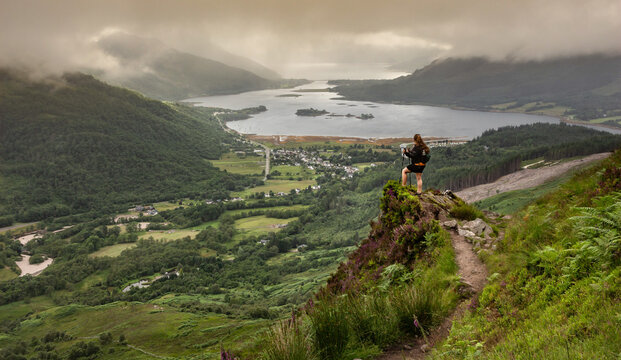 Woman standing on a rock with hiking poles overlooking the valley of Glencoe, Highlands of Scotland