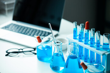 A laptop is on a table with a blue liquid in a beaker and a glass
