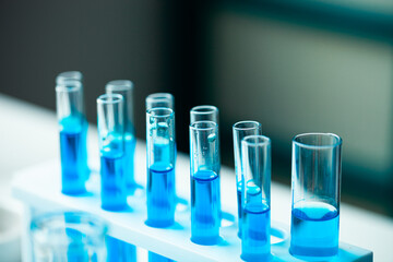 A row of blue test tubes are lined up on a white lab bench. The tubes are filled with clear liquid, and the overall mood of the image is one of scientific experimentation and discovery