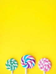 Three colorful lollipops against a bright yellow background. Vibrant candy pops and space to add personalized text