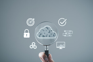 Hand holding magnifying glass with cloud computing icons, representing data analysis, storage, and security in a digital environment.