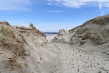 Zwischen hohen Dünen führt dieser offizielle Sandweg an den Strand der Nordseeinsel Norderney. Im Hintergrund branden Wellen bei ablaufendem Wasser an diesem sonnigen Frühlingstag.