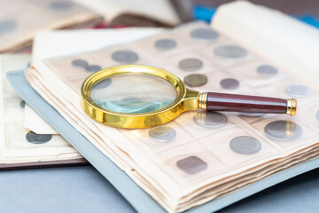 A close-up shot of a magnifying glass and a special crafted album with antique coins that a numismatics has just left
