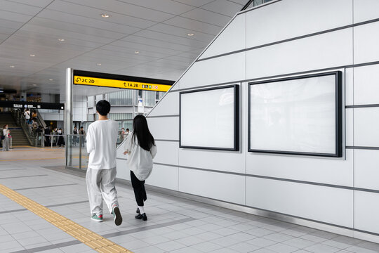 A young japanese couple walks in front of two blank billboard posters displayed down an escalator in a metro station in Tokyo. Ideal for advertising and mockup - Powered by Adobe