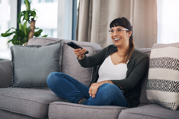 Obraz premium Woman, sofa and remote control for watching tv with smile for choice, comedy or subscription in home. Person, relax and happy on couch for streaming, movies or film with decision at house in Mexico