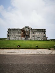 Once-grand colonial building in Battambang, Cambodia, now stands abandoned. Weathered facade, ornate balconies, and empty lawn create an atmospheric scene of faded glory.