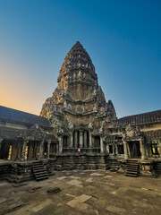 Iconic Angkor Wat temple in Cambodia, illuminated by evening light. Ancient stone structure with ornate carvings and towering central spire dominates the scene.