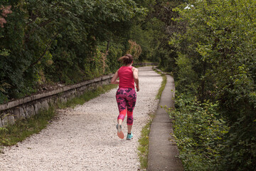 Obraz premium A young female athlete from behind is running on a countryside path