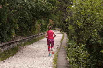 Obraz premium A young female athlete from behind is running on a countryside path