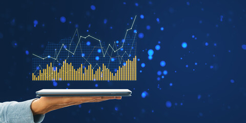 A hand holding a tablet displaying a holographic graph, with gold bars and lines on a dark blue background, concept of digital finance