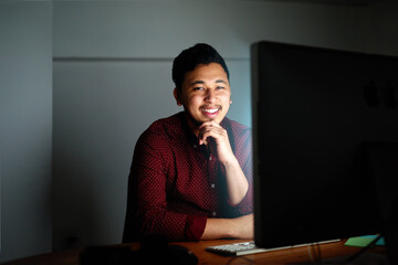 Smile, man and computer at night in office of coding, problem solving and software design as Developer. Male person, programmer and pc update with IT help for deadline maintenance by working late
