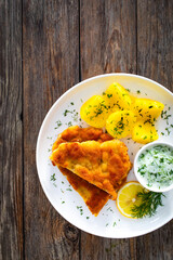 Crispy breaded seared chicken cutlet with boiled potatoes and cucumbers in cream served on white plate on wooden table