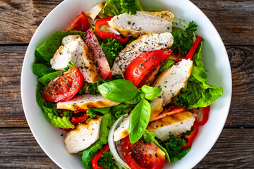 Caesar style salad - delicious grilled chicken breast slices and fresh vegetables and seasonings served in white bowl on wooden table
