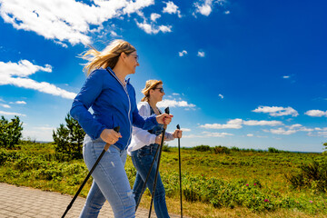 Nordic walking - two mid-adult beautiful women in casual clothing exercising on footpath in city...
