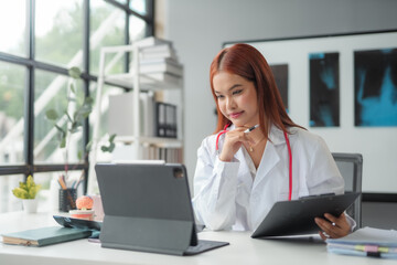 Young doctor working with medical records on tablet in her office