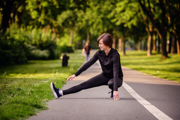 A young woman in black athletic wear stretching her legs on a park path before jogging. Emphasizing warm-up exercises and a healthy outdoor lifestyle.