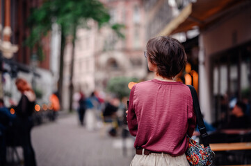 Woman in casual attire with a colorful backpack walking through a bustling city street filled with people and cafes.