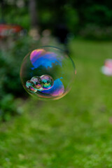 Big colorful blue soap bubble on green background in the garden blown and made by kids