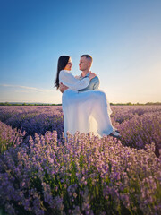 Fototapeta premium Young couple hugging together on a date in the lavender field. Picturesque summer scene, marriage love and romance concept