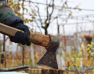 male hands in black gloves hold an ax for chopping wood. autumn preparation of firewood before the winter cold. ecological material for heating with a fireplace or stove