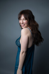Naklejka premium Studio portrait of a beautiful caucasian woman in her 30s wearing a dark blue night gown. She is smiling and looking at the camera. The studio background is grey. 