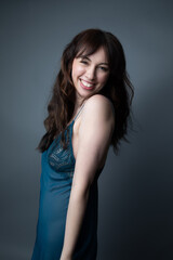 Fototapeta premium Studio portrait of a beautiful caucasian woman in her 30s wearing a dark blue night gown. She is smiling and looking at the camera. The studio background is grey. 