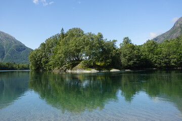 Mountain river and nature of Norway. Summer and sunny day. Forest on stones, white clouds in the mountains. Blue sky