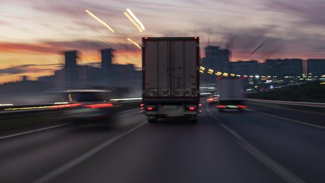 Time lapse of speedy truck with semi-trailer driving on highway along big city in evening time at sunset, rear view of cargo van.