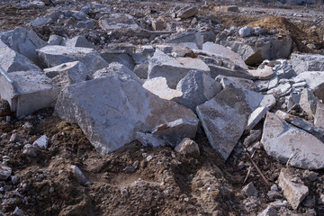 A pile of large gray concrete fragments of the remains of the building are scattered on the ground during the demolition of the building structure. Background