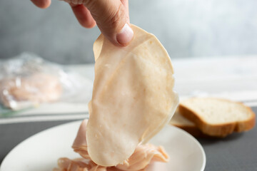 A closeup view of a hand holding a  single piece of processed turkey deli meat slices.