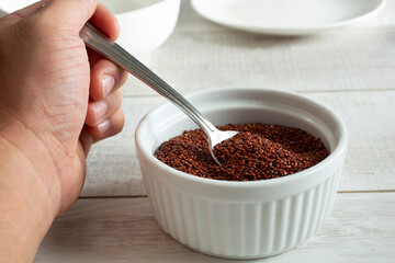 A view of a hand using a spoon to scoop some raw red quinoa from a bowl.