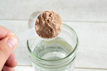 A view of a hand pouring a scoop of protein powder into a glass of water.