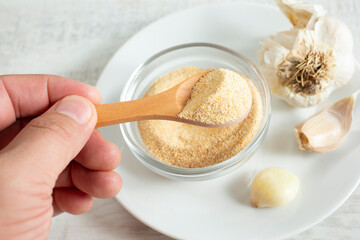 A view of a hand using a small wooden spoon to scoop some granulated garlic from a condiment cup.