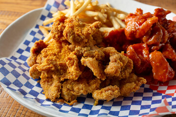 A closeup view of a platter of two kinds of Korean fried chicken, with french fries.