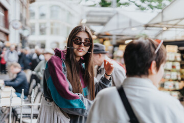 Young woman in stylish sunglasses at an urban market engaging with a friend, creating a lively social atmosphere.