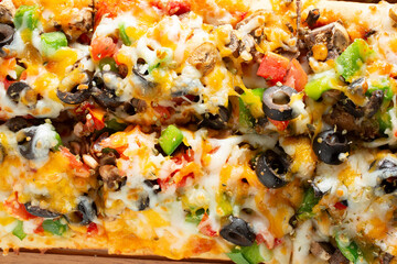 A top down view of a veggie flatbread, featuring toppings as black olives, bell peppers and cheese.