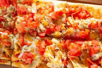 A top down view of a flatbread appetizer, featuring toppings as chicken, tomato and cheese.