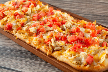 A view of a flatbread appetizer, featuring toppings as chicken, tomato and cheese.